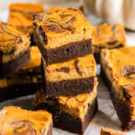 stack of three fudgy pumpkin cheesecake brownies next to some more brownies.