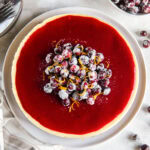 tabletop with cranberry cheesecake topped with glossy cranberry glaze and sugar cranberries.