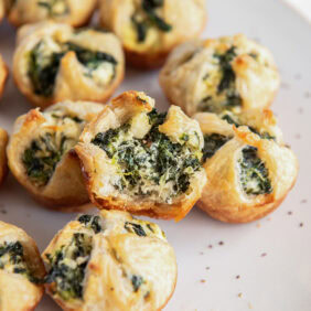 spinach puff with a bite sitting on plate with more spinach puffs.