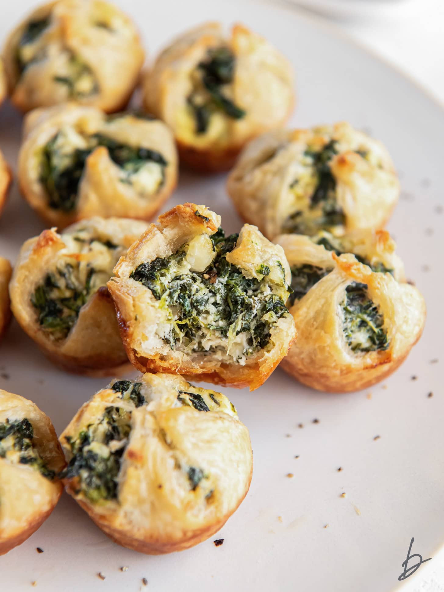 spinach puff with a bite sitting on plate with more spinach puffs.