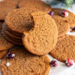 thin gingersnap cookie with bite taken out of it leaning on stack of more cookies.
