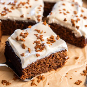 parchment paper with square slice of gingerbread sheet cake with maple frosting.