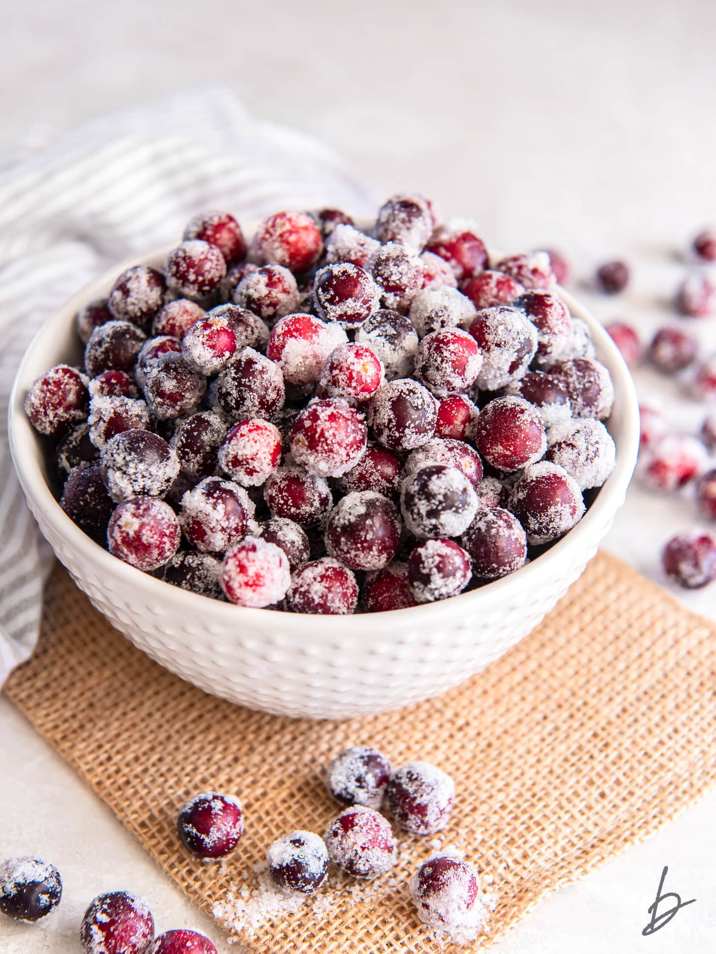 bowl of sugared cranberries on a tabletop with placemat and more sugared cranberries.