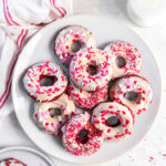 tabletop with plate of red velvet donuts with cream cheese icing and valentine's day sprinkles.