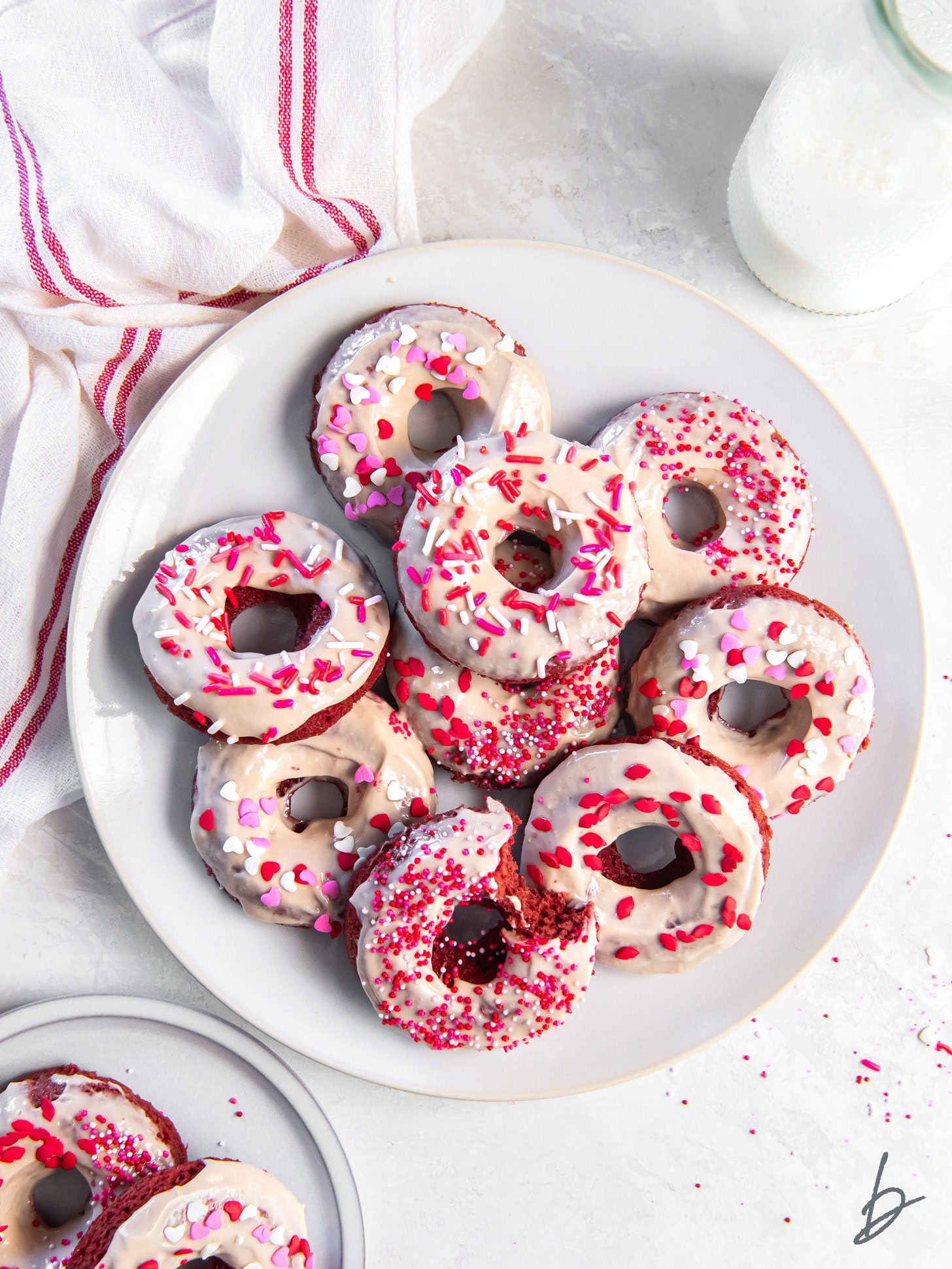 tabletop with plate of red velvet donuts with cream cheese icing and valentine's day sprinkles.