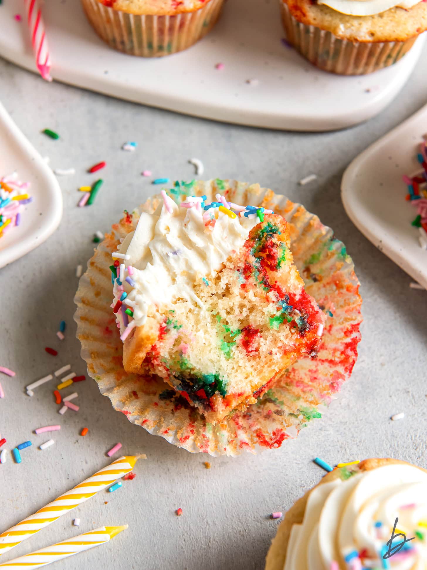 open paper cupcake liner with a funfetti cupcake that has a bite taken out of it.