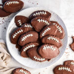 chocolate football cookies on a plate on a tabletop with a few more cookies.