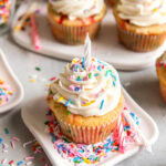 small plate with funfetti cupcake topped with vanilla frosting, sprinkles and a birthday candle.