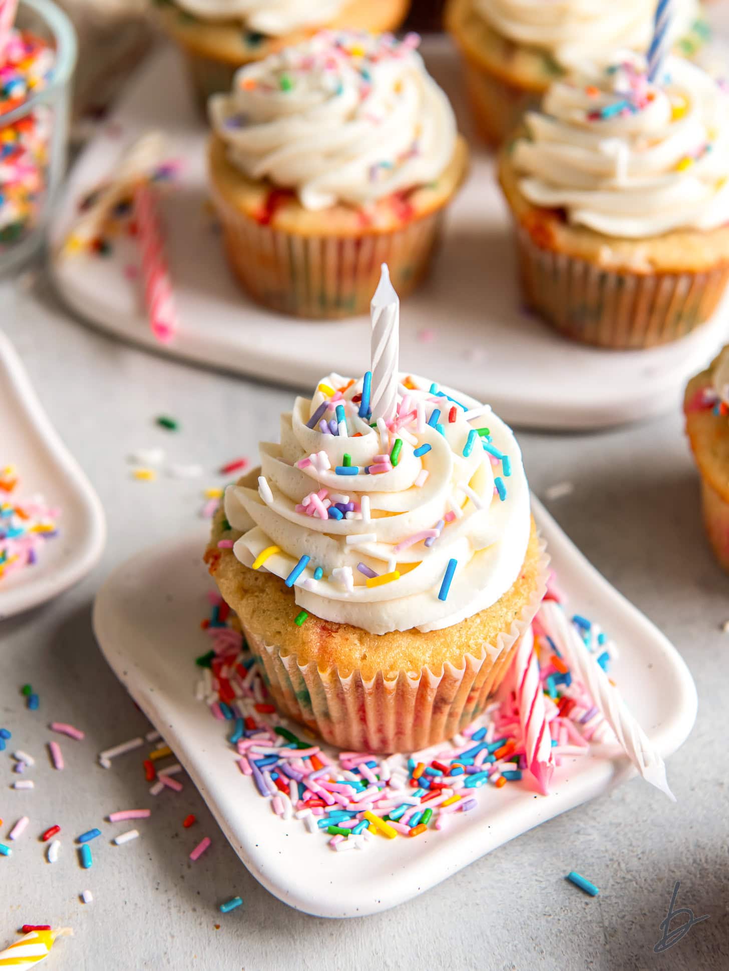 small plate with funfetti cupcake topped with vanilla frosting, sprinkles and a birthday candle.