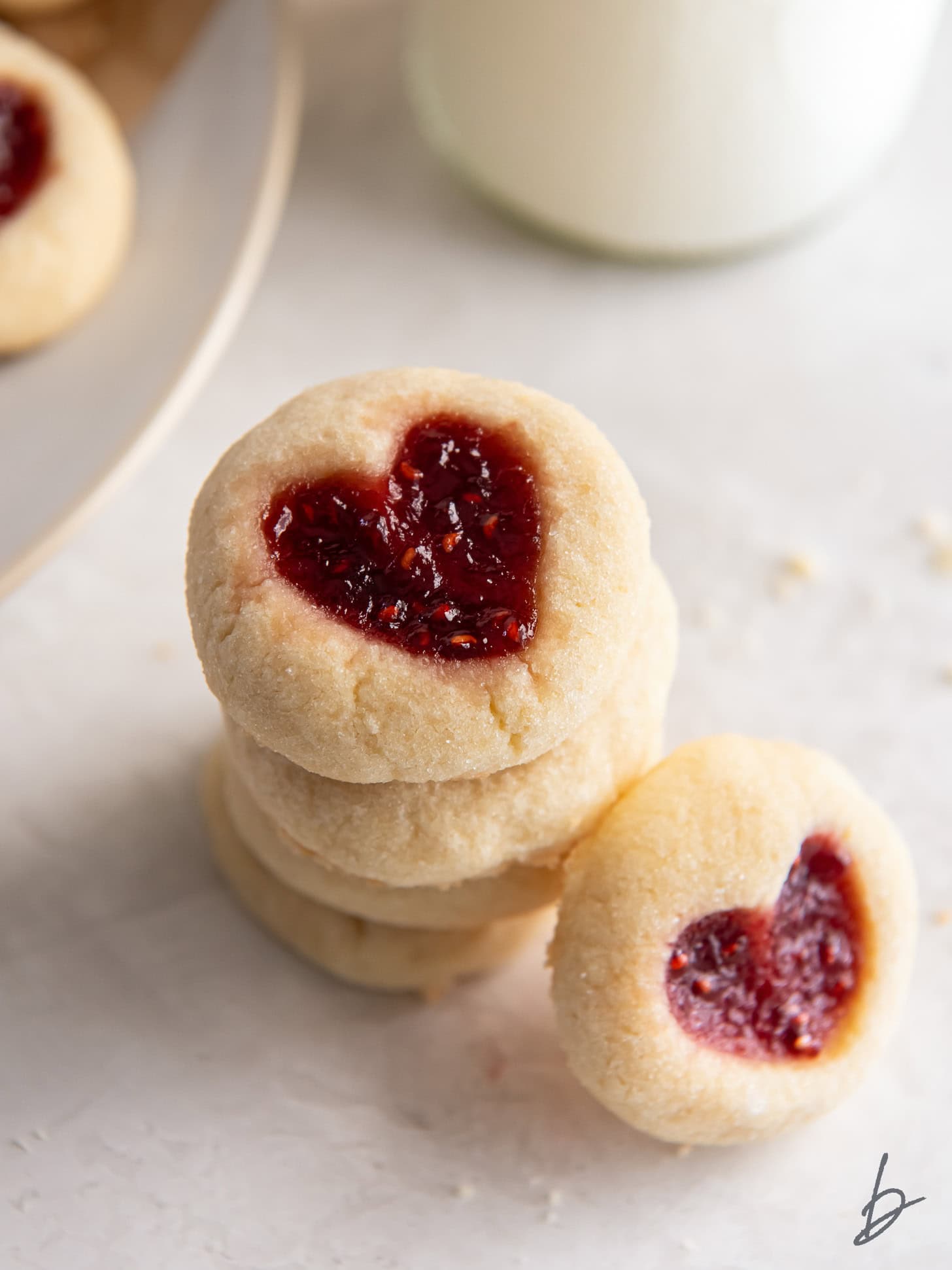 stack of thumbprint heart cookies with jam and one cookie leaning on stack.