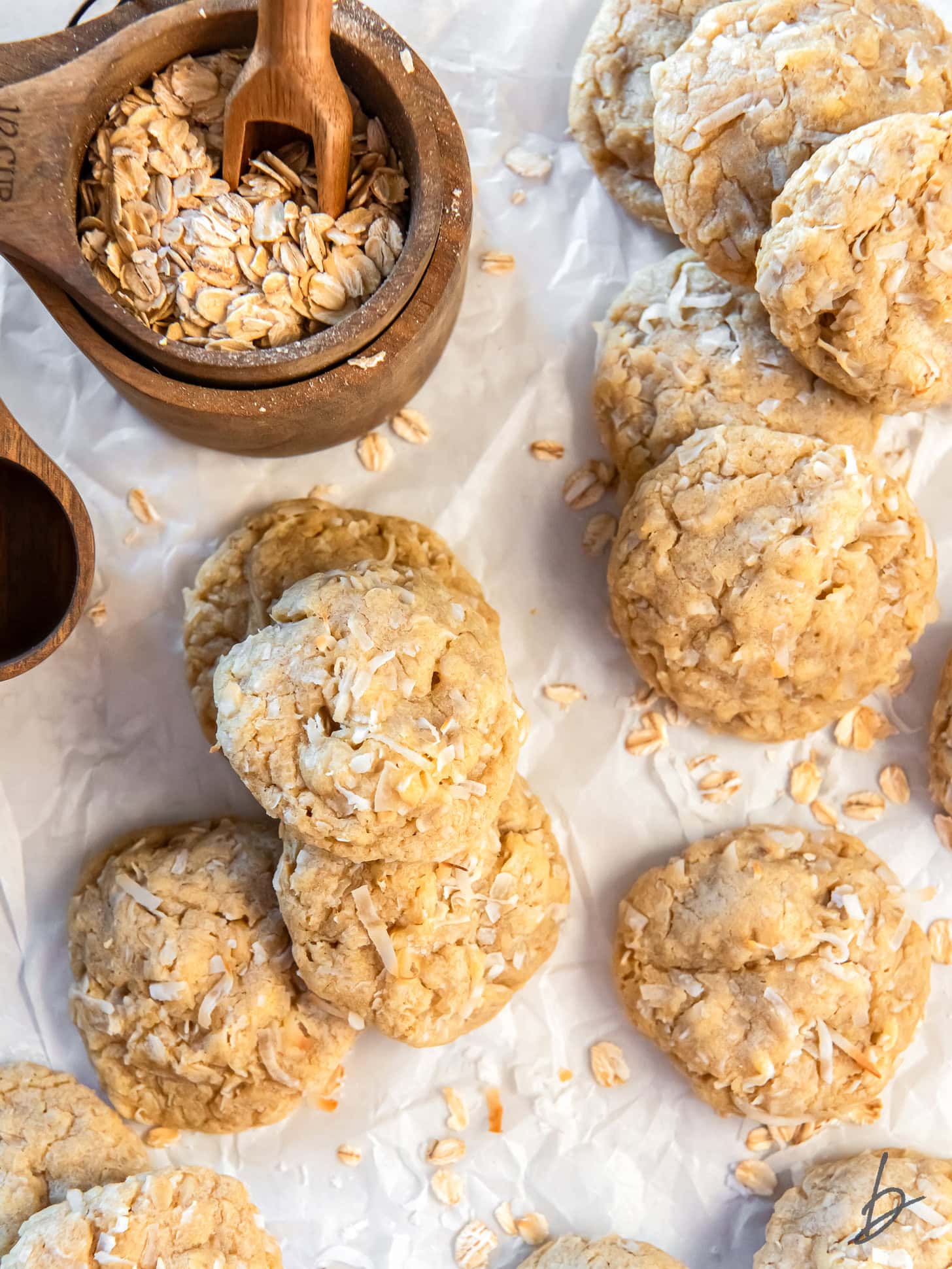 oatmeal coconut cookies on a tabletop next to a small wooden bowl with rolled oats.