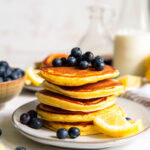 Lemon Ricotta Pancakes topped with blueberries stacked on a white plate.