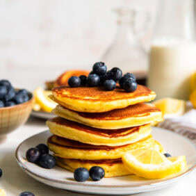 Lemon Ricotta Pancakes topped with blueberries stacked on a white plate.