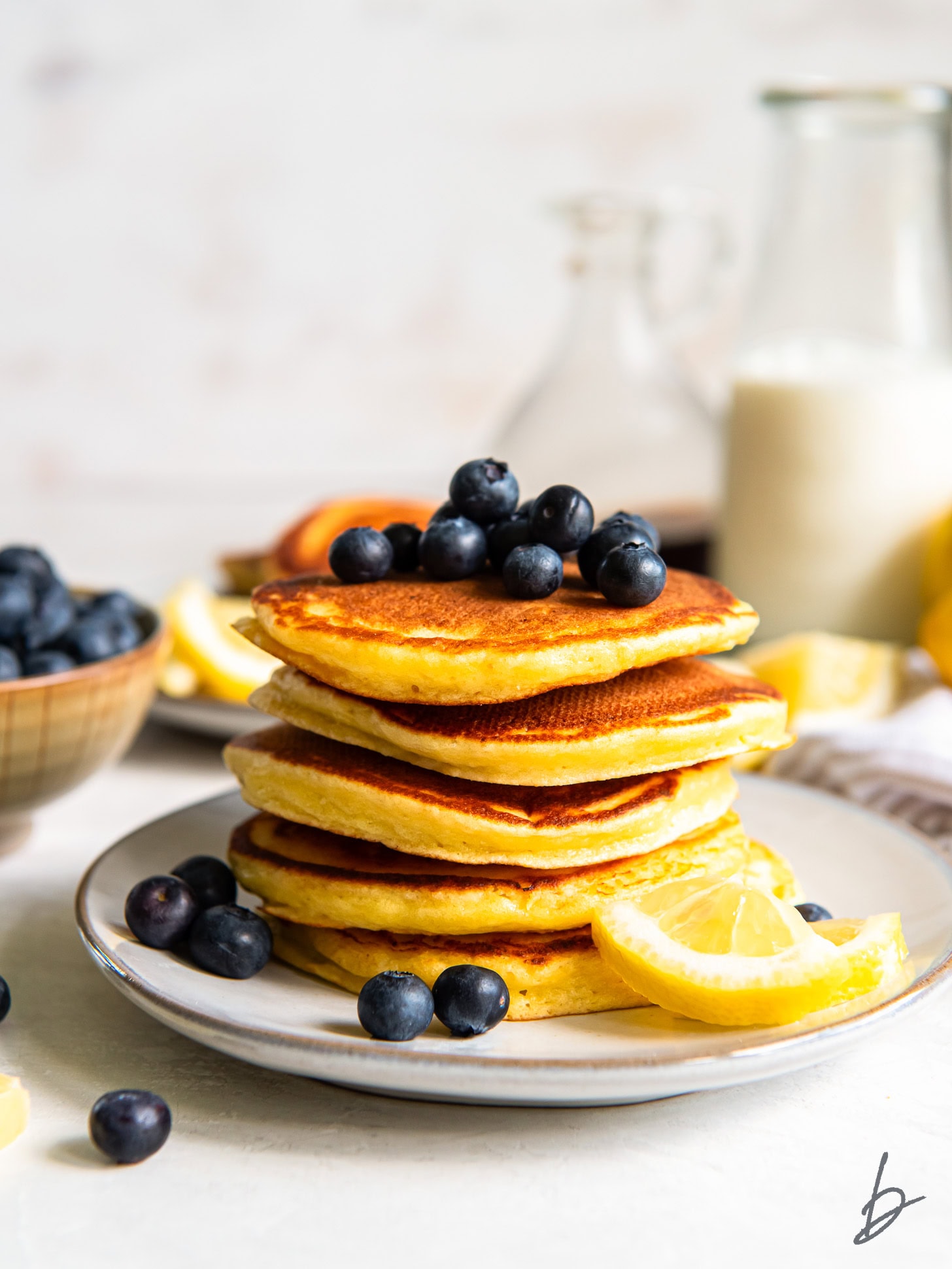 Lemon Ricotta Pancakes topped with blueberries stacked on a white plate.