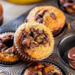 nutella swirl on top of a banana nutella muffin leaning on muffin in muffin tin.