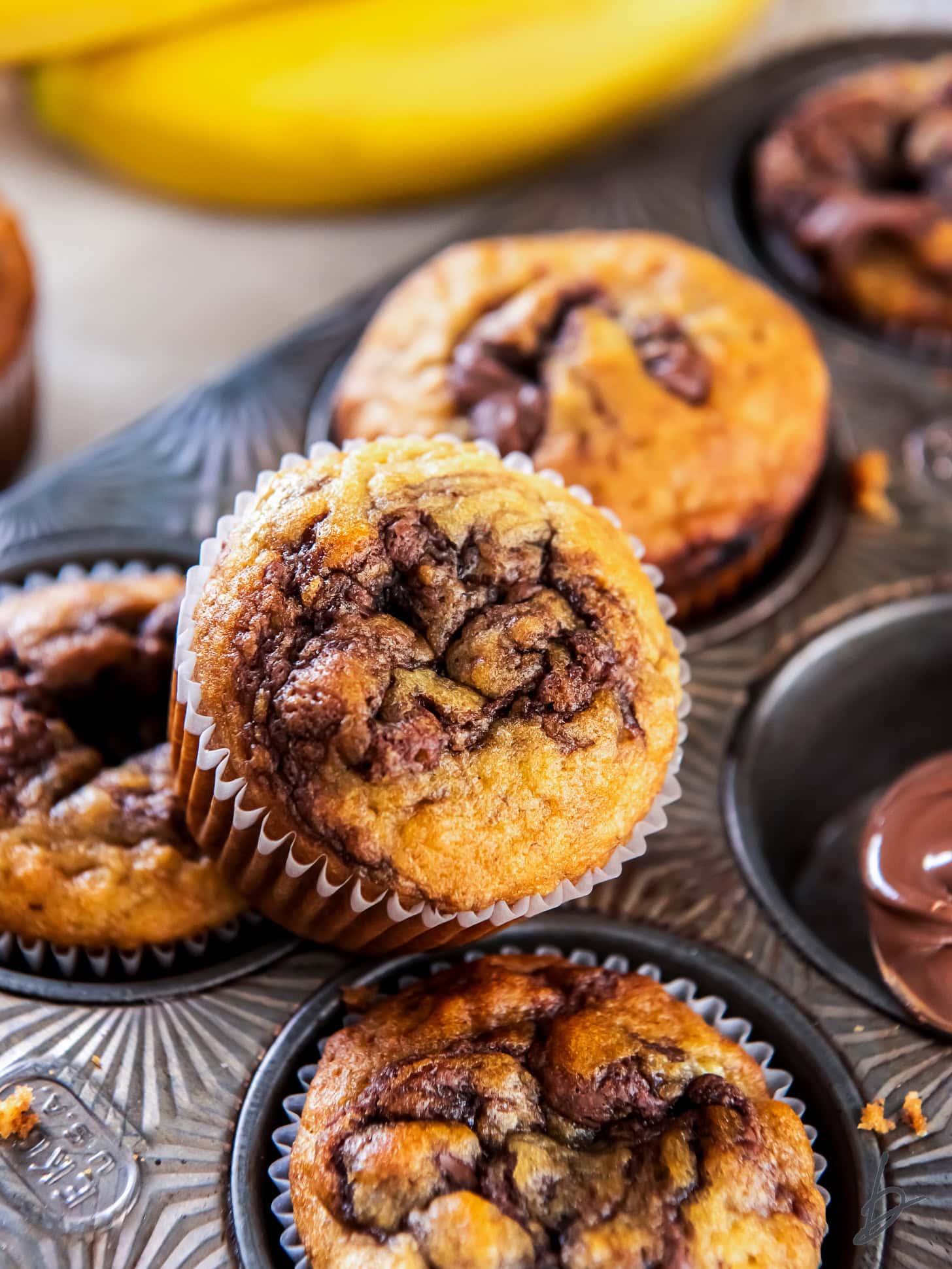nutella swirl on top of a banana nutella muffin leaning on muffin in muffin tin.