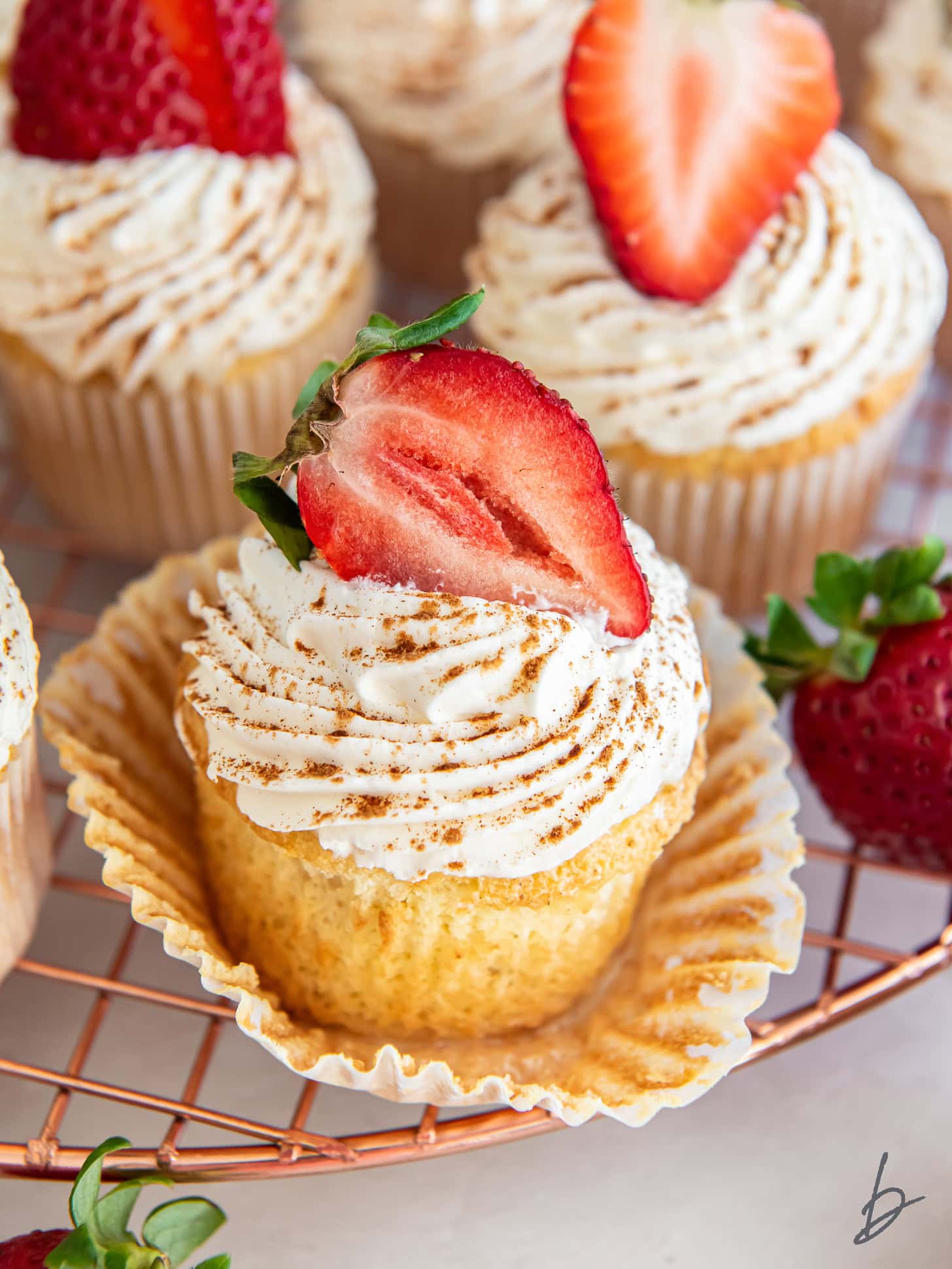 tres leches cupcake with whipped topping and strawberry garnish on open paper liner.