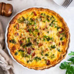 broccoli quiche on a tabletop next to a couple plates and forks.