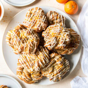 Knotted cardamom rolls with icing on a white plate.