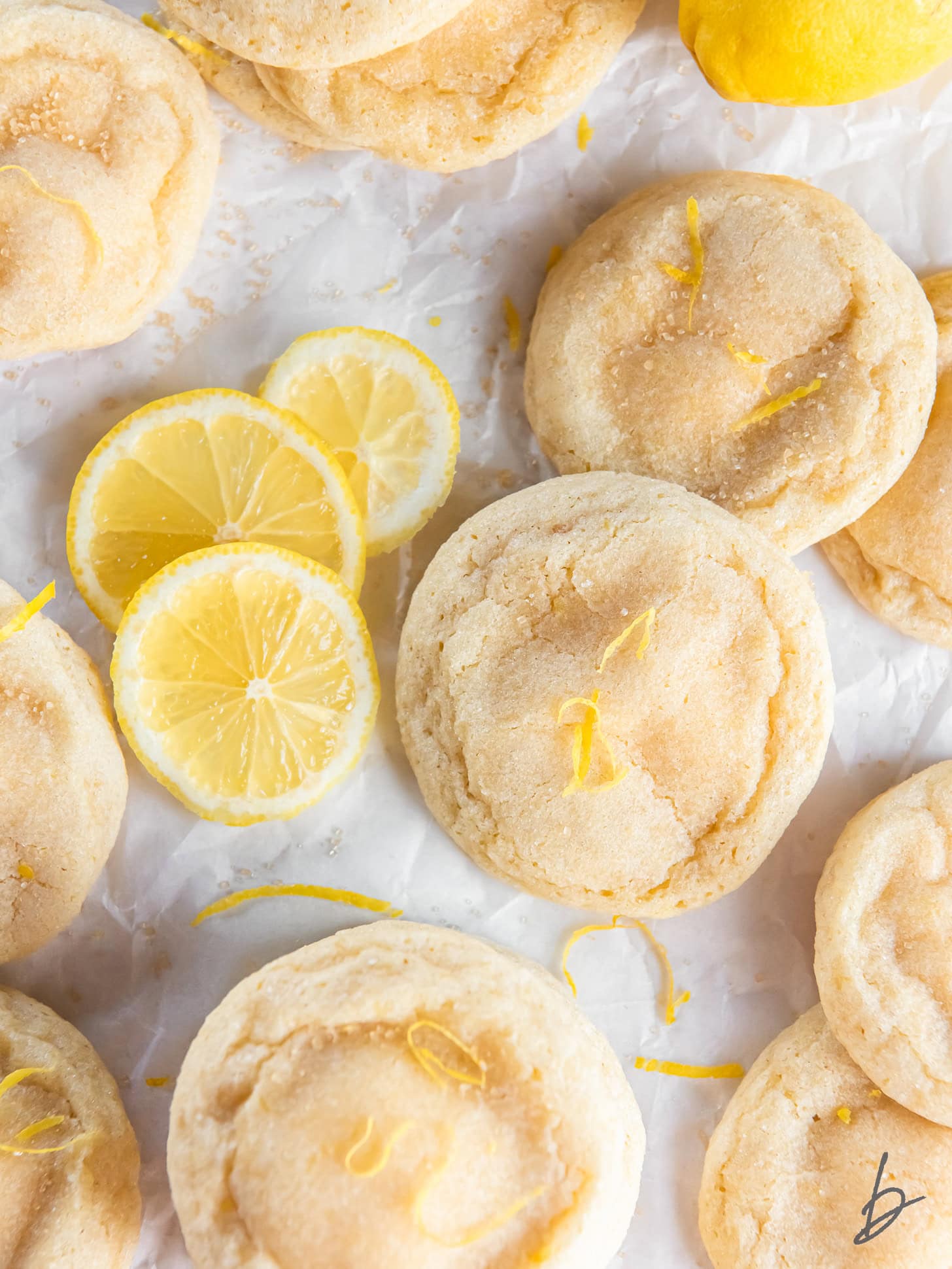 lemon cheesecake cookies on parchment paper with a few lemon slices.