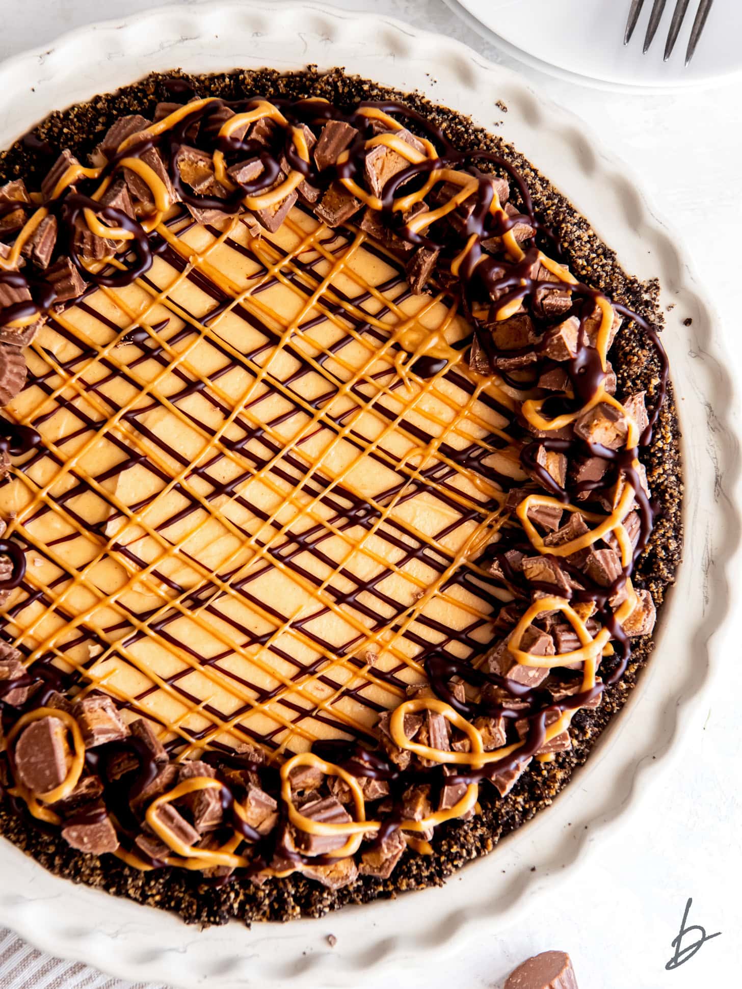 Peanut butter pie topped with chocolate and peanut butter drizzle and decorated with mini Reese's.