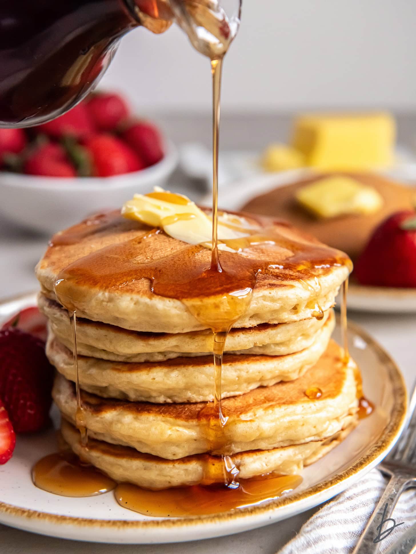 syrup poured over and dripping down stack of fluffy buttermilk pancakes.