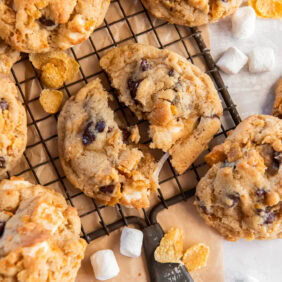 tabletop with wire cooling rack and a milk bar cornflake cookie pulled apart to show gooey marshmallows.