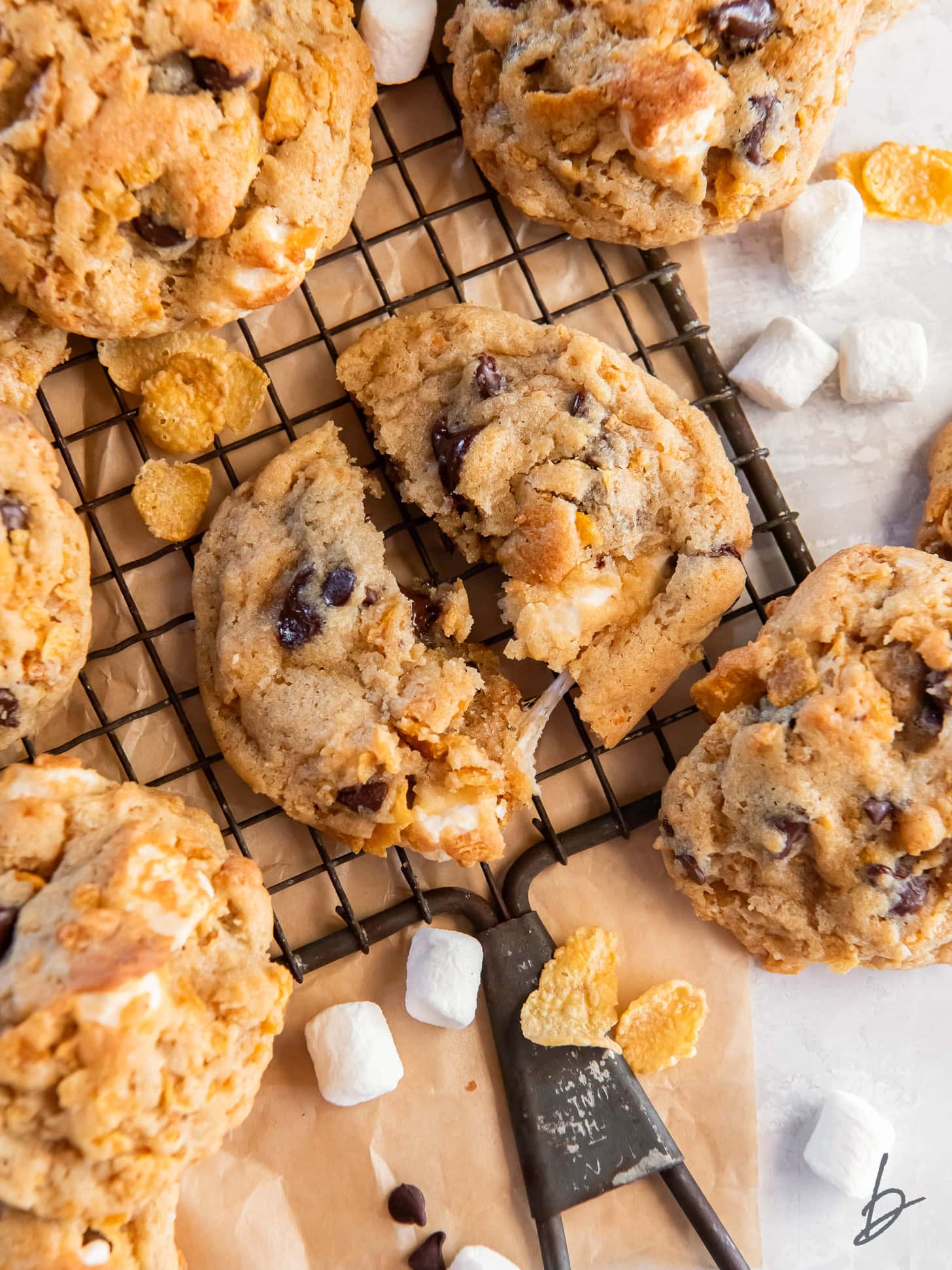 tabletop with wire cooling rack and a milk bar cornflake cookie pulled apart to show gooey marshmallows.