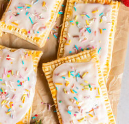 homemade strawberry pop tarts on parchment paper on tabletop with a couple strawberries.