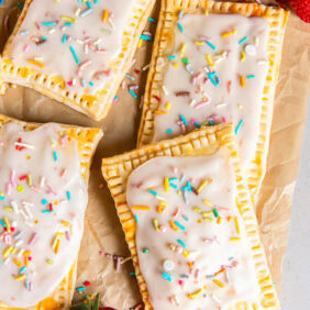 homemade strawberry pop tarts on parchment paper on tabletop with a couple strawberries.