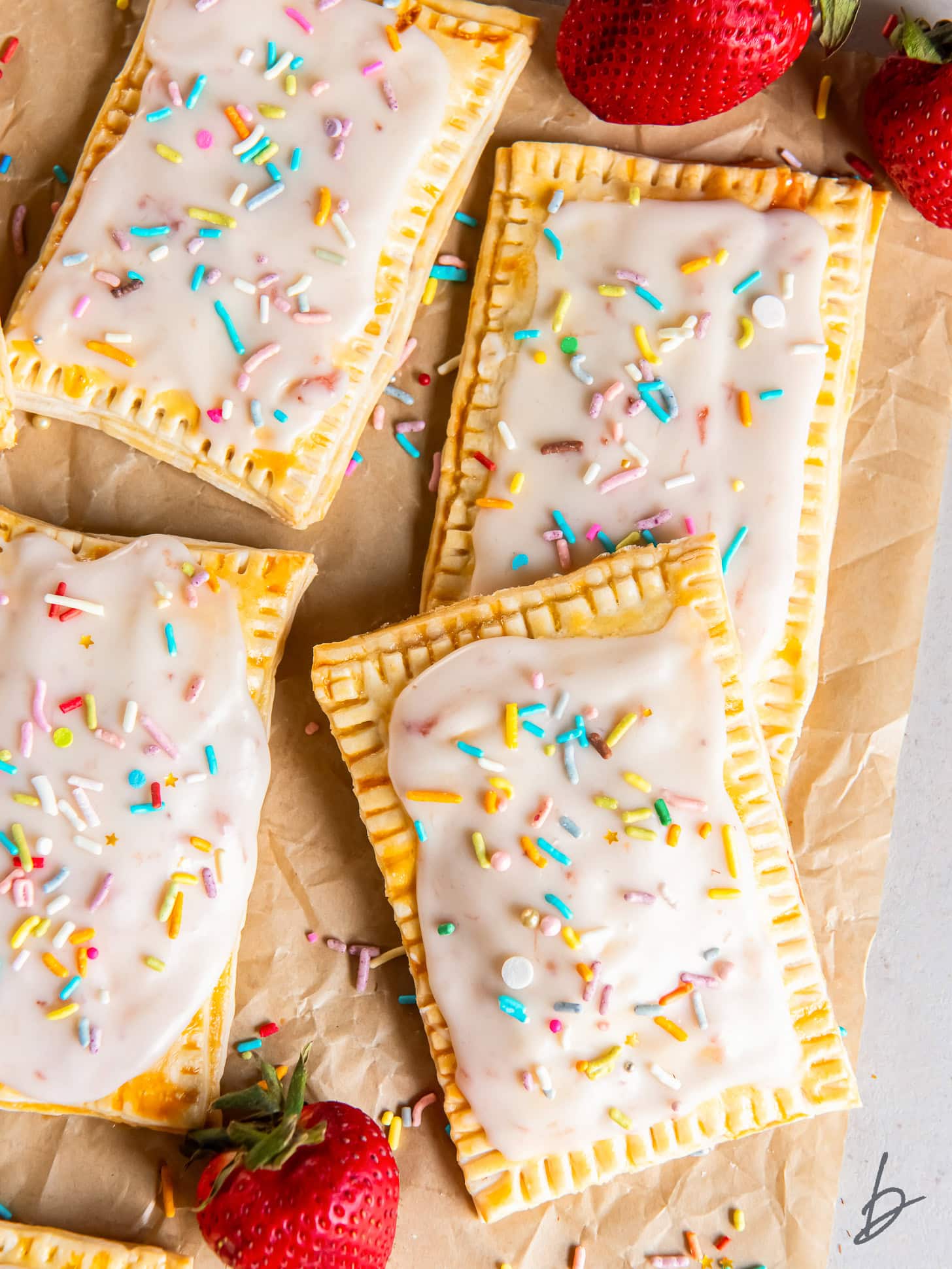 homemade strawberry pop tarts on parchment paper on tabletop with a couple strawberries.