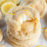 stack of lemon cheesecake cookies and top cookie has a bite showing cheesecake inside.