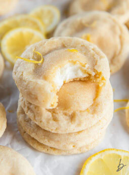 stack of lemon cheesecake cookies and top cookie has a bite showing cheesecake inside.