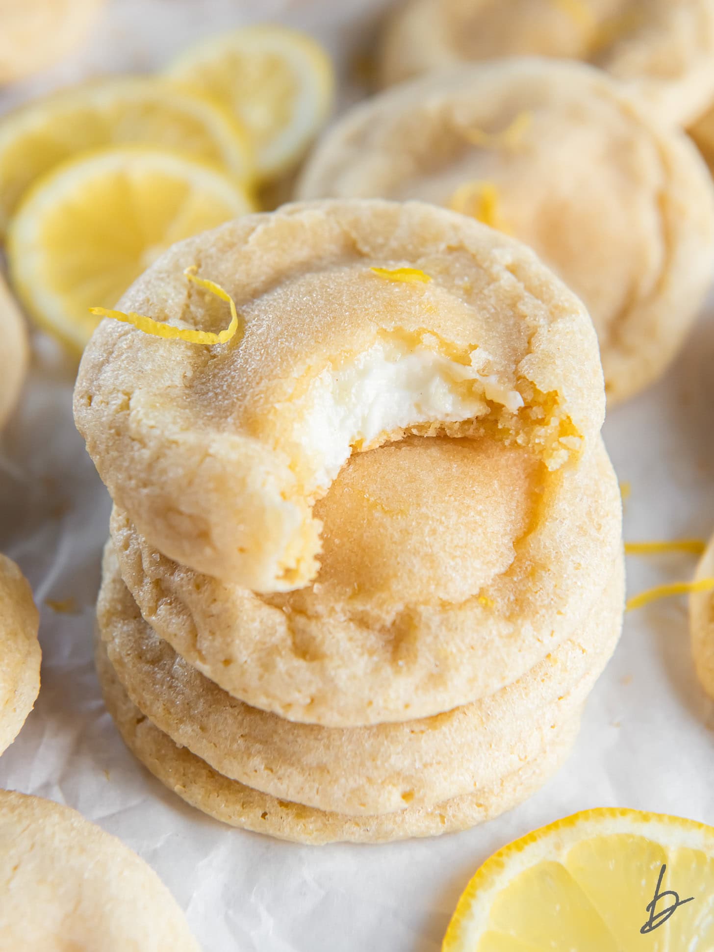 stack of lemon cheesecake cookies and top cookie has a bite showing cheesecake inside.