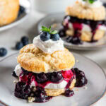 plate with blueberry shortcake garnished with a dollop of whipped cream, fresh blueberries and sprig of mint.