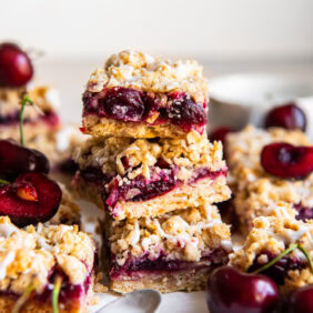 stack of three cherry crumb bars surrounded by more bars and fresh cherries.