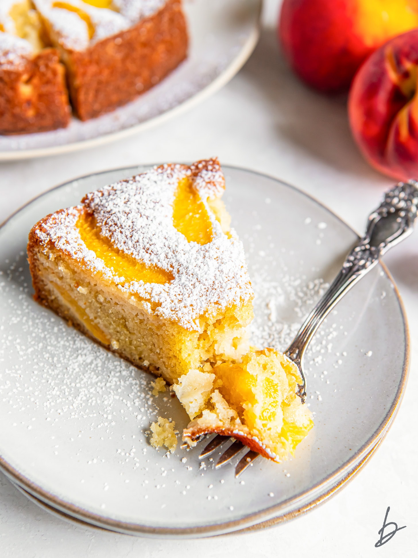slice of fresh peach cake on a plate and a fork taking a bite.