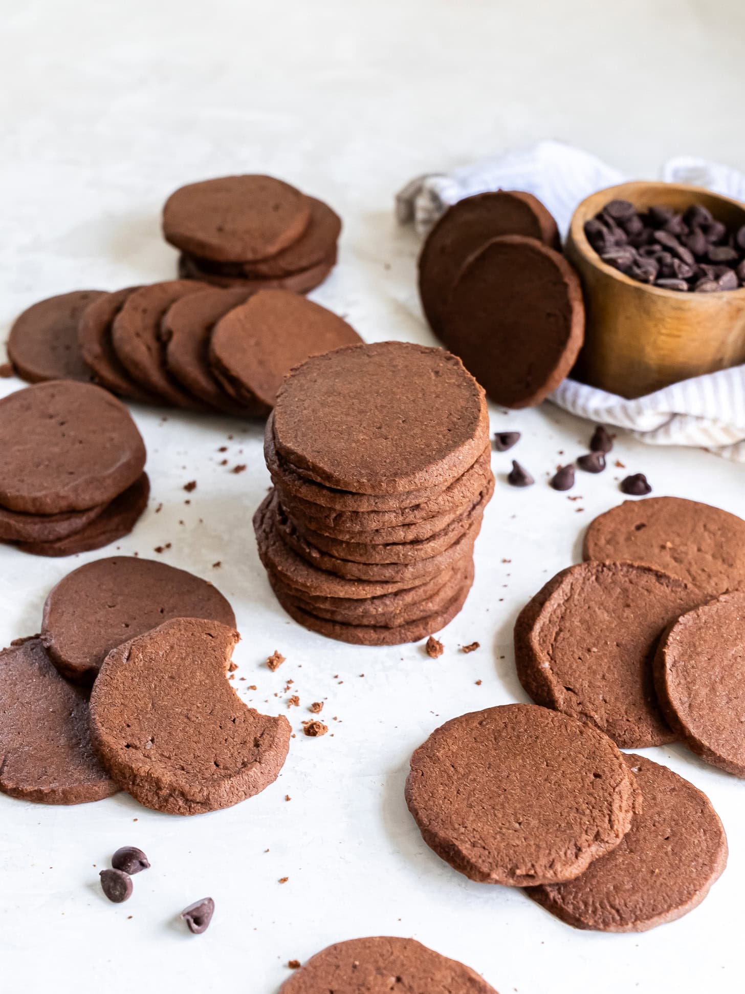 chocolate icebox cookies in a stack next to more cookies scattered on a tabletop.