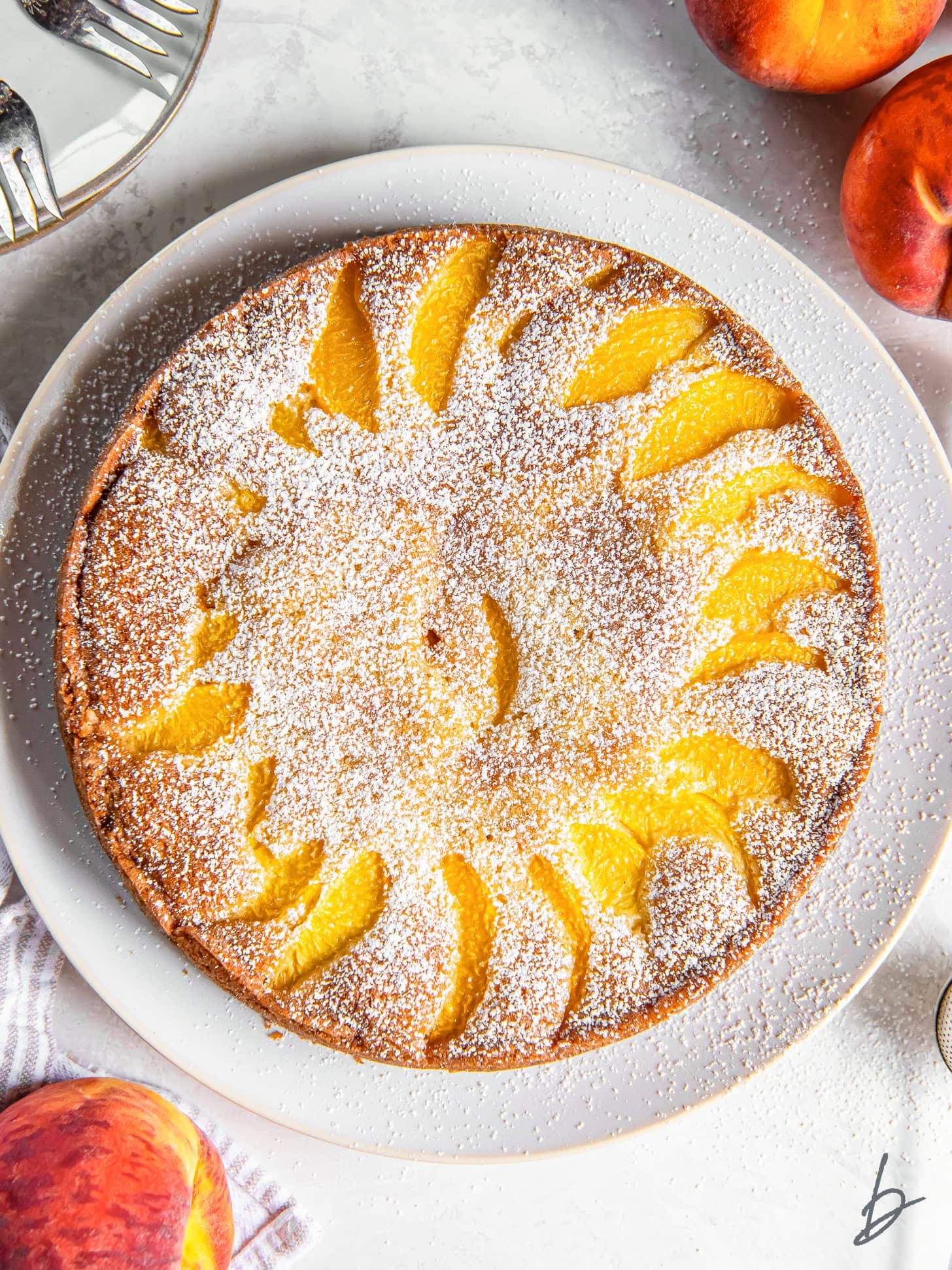 tabletop with plate of fresh peach cake dusted with confectioners' sugar.