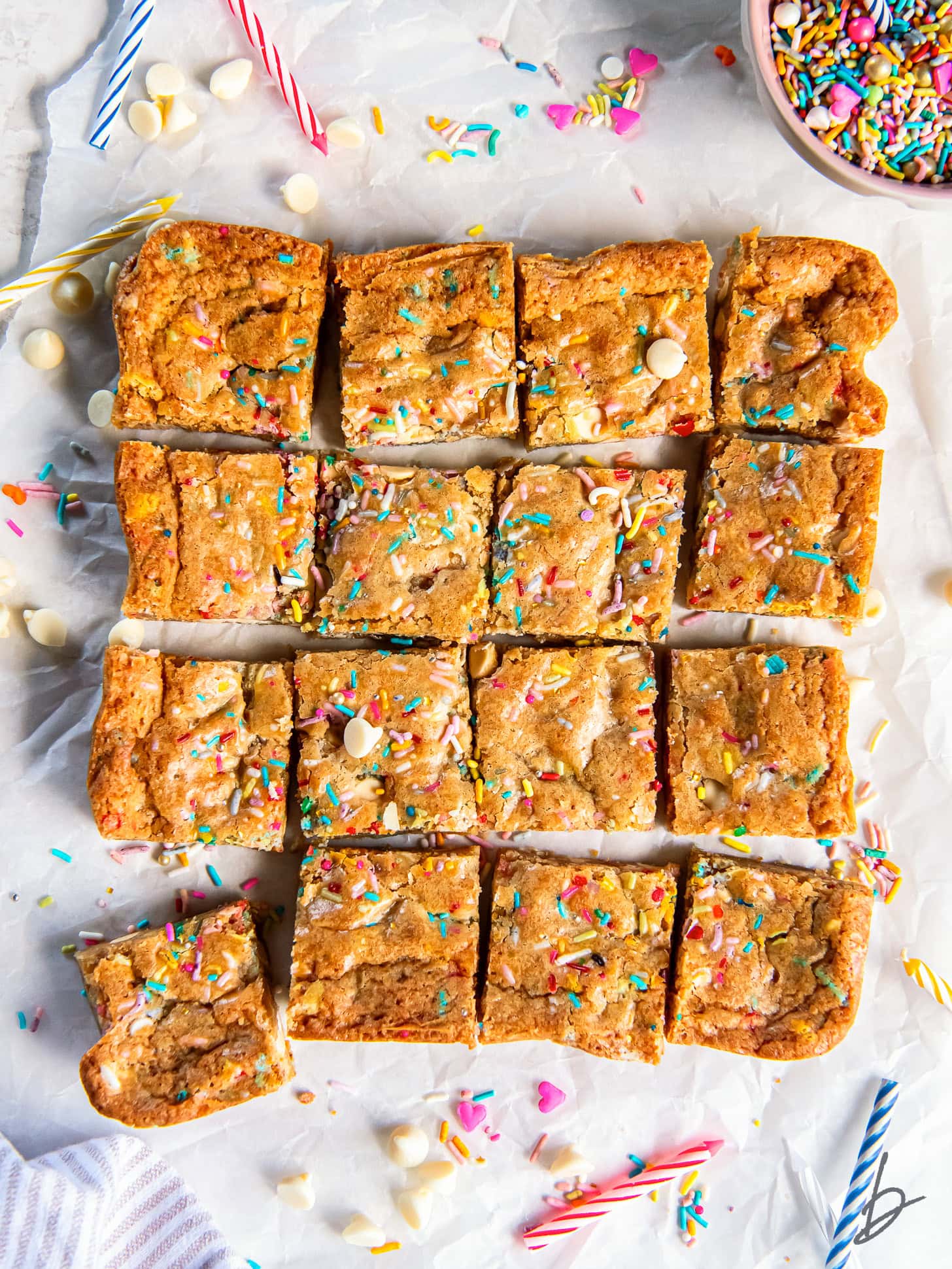 tabletop with birthday cake blondies cut into squares on parchment paper.