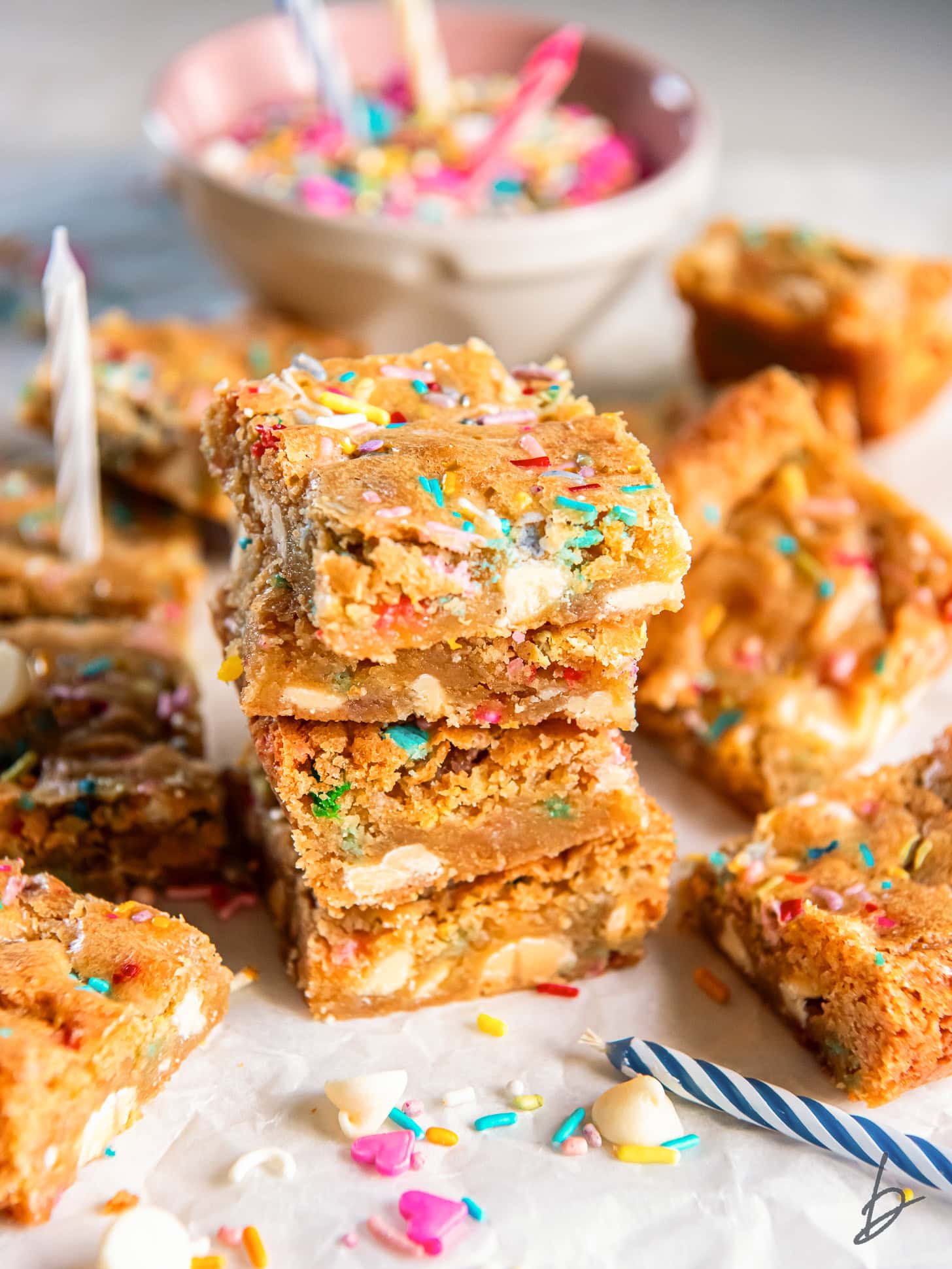 stack of four birthday cake blondies in front of some more blondies and sprinkles.