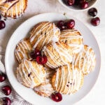 tabletop with plate of cherry hand pies with glaze next to a few fresh cherries.
