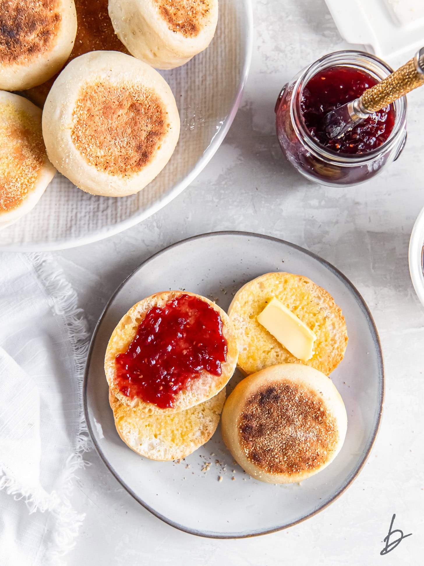 English muffins topped with butter and jam on a plate.