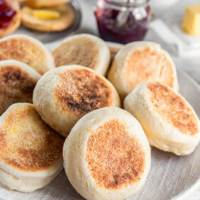 Homemade English muffins stacked on a plate.
