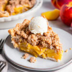 Slice of peach crumble pie topped with vanilla ice cream.