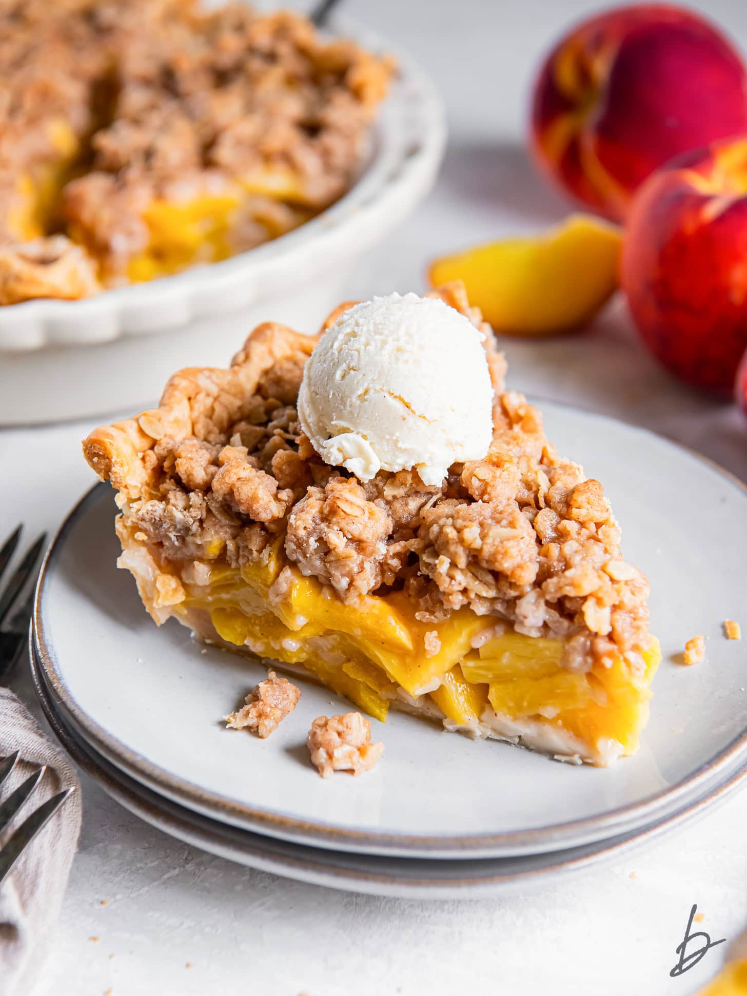 Slice of peach crumble pie topped with vanilla ice cream.
