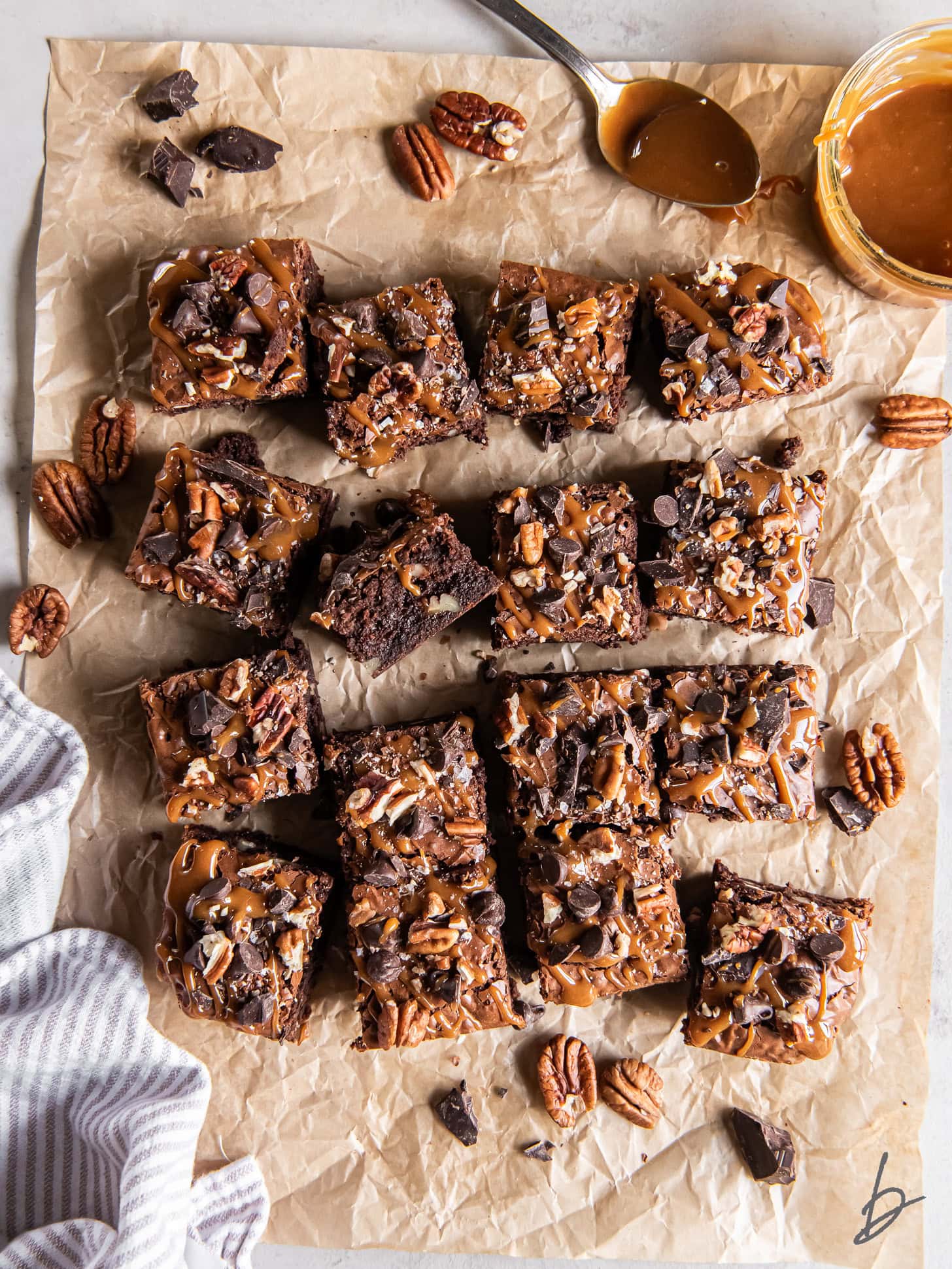 Sliced brownies on parchment paper near a small bowl of caramel sauce.