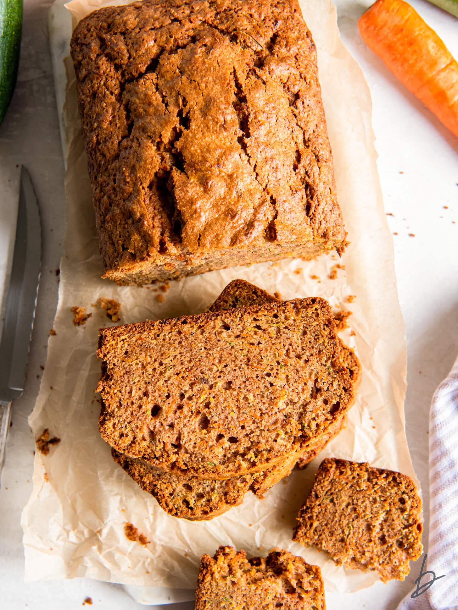 tabletop with loaf of zucchini carrot bread next to stack of a couple slices.