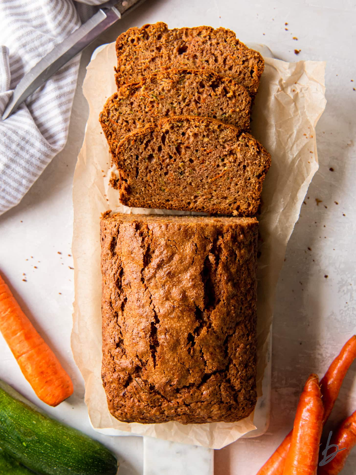 tabletop with loaf of zucchini carrot bread with three slices cut off the end.