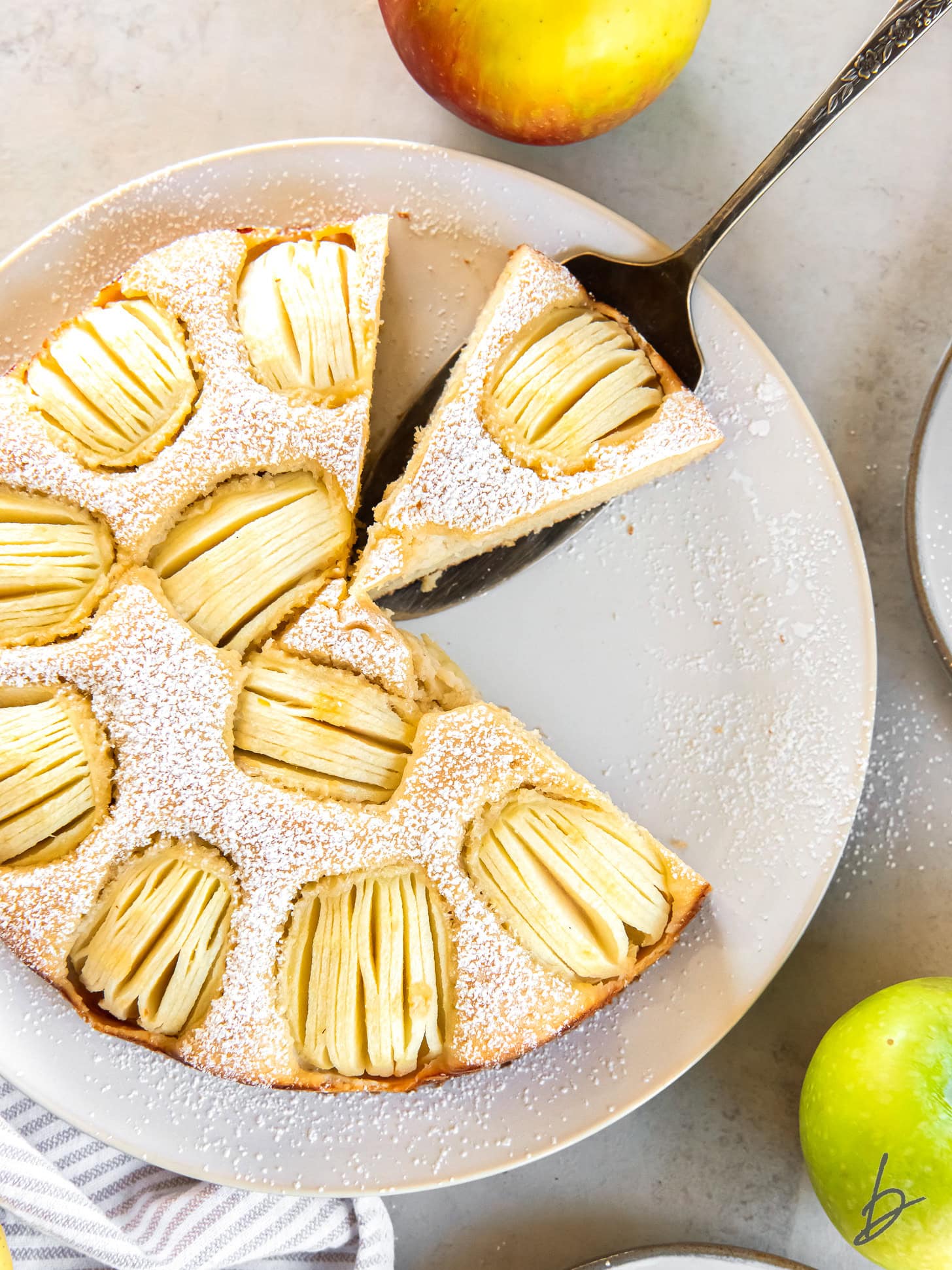 Serving a German apple cake from a large white serving plate. 